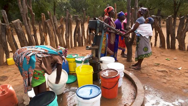 Water shortage. Six woman and a baby drawing water into plastic containers from a communal water pump,Zimbabwe