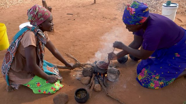 Two woman cooking sorghum in traditional clay pots on a small open fire, Zimbabwe