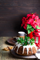 Christmas chocolate cake with white icing and pomegranate kernels on a wooden dark background with red lantern and poinsettia