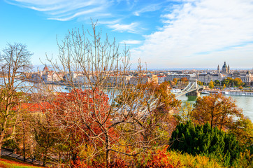 Fall trees in the foreground with the amazing cityscape of Budapest, Hungary in the background. Hungarian Parliament Building with Danube river. Autumn tree branches and foliage. Capital city