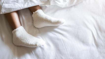 Woman feet in warm woolen socks on white bedclothes. Close up of young woman lying in bed at home. Relaxing concept.