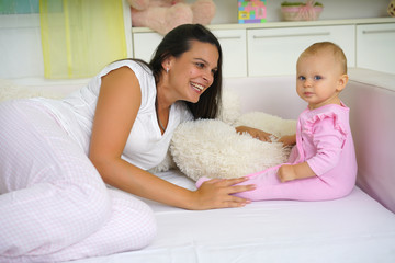   Smiling mom and baby sitting in bed, baby looking at camera        