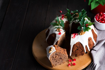 Christmas chocolate cake with white icing and pomegranate kernels on a wooden dark background with red lantern and poinsettia