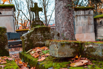 Stone cross in the most famous cemetery of Paris Pere Lachaise, France. Tombs of various famous people. Golden autumn over eldest tombs.