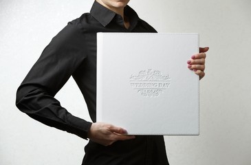 a woman holds a square family photobook. the person looks at the photo book. sample  white photo album in womans hands .wedding photoalbum with   leather cover.