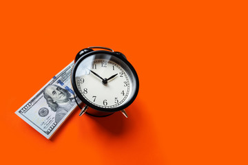 Alarm clock lying on a stack money on orange background with copyspace. Stack of hundred dollars