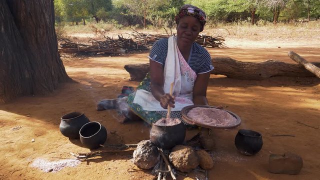 A woman cooking sorghum in traditional clay pots on a small open fire, Zimbabwe