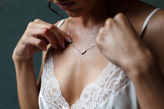 Girl in a white dress with a  silver chain around her neck. The bride fixes a decoration of a jewel on the neck. Stylish fashionable diamond suspension. girl's neck pendant. pendant for women's neck.