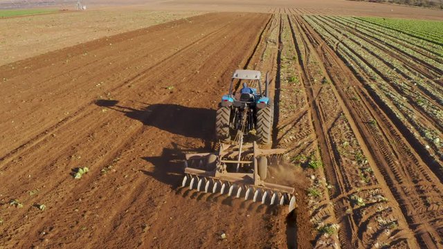 Aerial close-up rear view of a tractor ploughing fields on a large scale farm