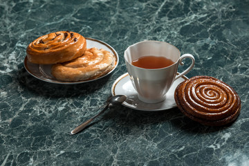cinnamon bun, Bun with raisins, with saucer, black tea and spoon on background