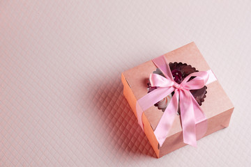 A square gift box with a pink ribbon on a light pink background. Cupcakes inside. Space for text, view from above