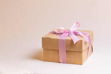 A square gift box with a pink ribbon on a light pink background. Cupcakes inside. Space for text, view from above