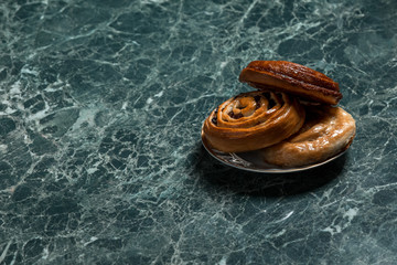cinnamon bun, Bun with raisins, meat pie on saucer on green marble background