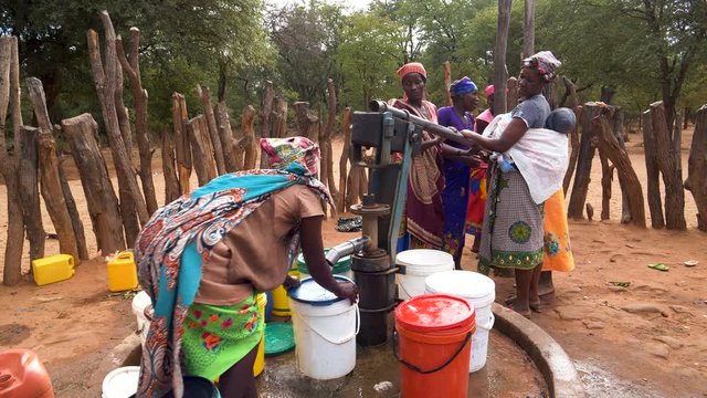 Water crisis. Six woman drawing water into plastic containers from a communal water pump, Mahenye Village, Zimbabwe