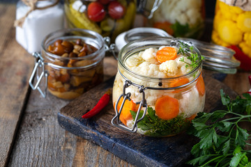 Pickled cauliflower with carrots in a glass jar on a dark wooden table. Fermented food