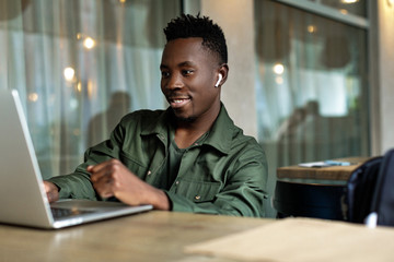 Cheerful young african american man in headphones using computer in cafe