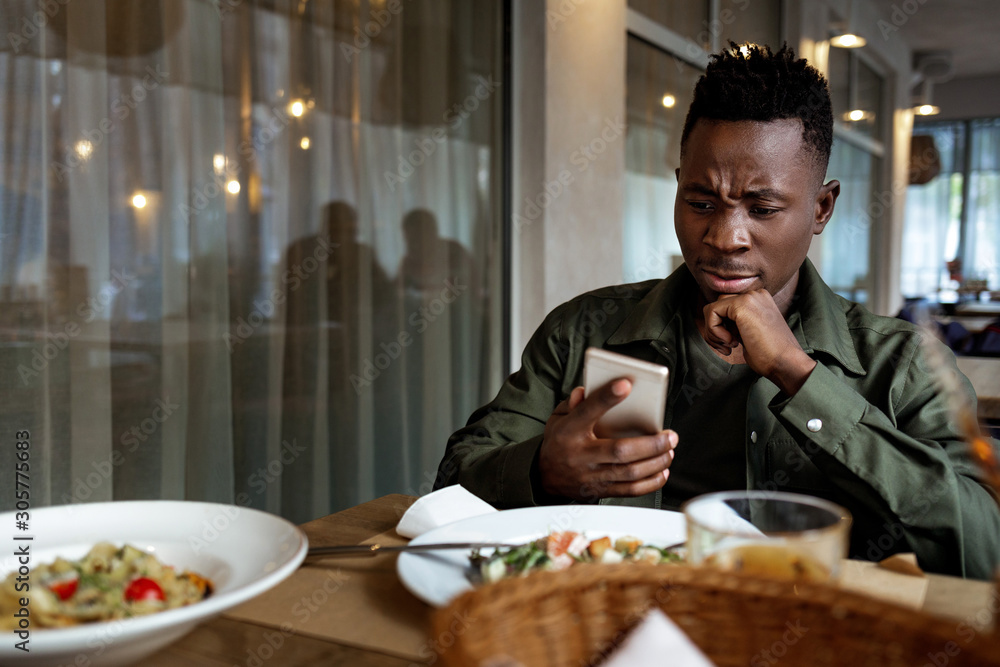 Wall mural young african american man messaging online, checking social networks in cafe. copy space