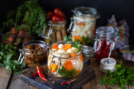 Pickled cauliflower with carrots in a glass jar on a dark wooden table. Fermented food