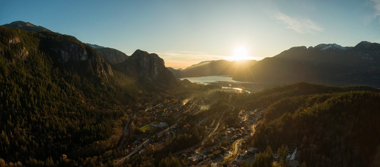 Obraz premium Squamish, North of Vancouver, British Columbia, Canada. Beautiful Aerial Panoramic View from the top of the Mountain of a small town surrounded by Canadian Nature during Autumn Sunset.