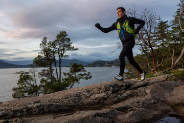 Adventurous Latino Male is Trail Running outdoors in Canadian Nature during sunset. Taken in Lighthouse Park, West Vancouver, BC, Canada. Funny Face