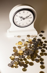 Fototapeta na wymiar White desk clock on a white background near scattered coins or 