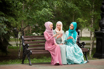 Fototapeta premium three beautiful young women in muslim dresses in the summer in the park with phones in their hands