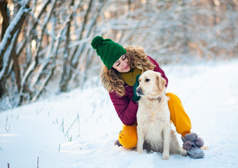 Smiling woman hugging her pet dog golden retriever near face. Golden retriever playing with a woman walking outdoors winter day, warm clothing. love and care for the pet.