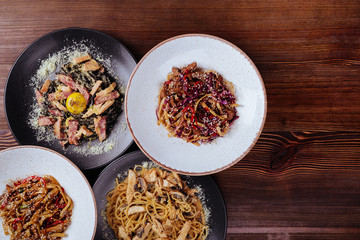 Several plates of pasta with different kinds of sauce over wooden background, top view. Concepts of Italian food.