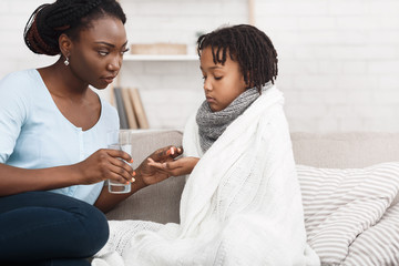 Black mom giving medicine for flu to child - obrazy, fototapety, plakaty