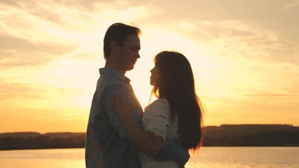 Young couple dancing at sunset on beach. Loving man and woman dance in bright rays of sun on background of the lake. Happy guy and girl waltz in the evening in the summer park.