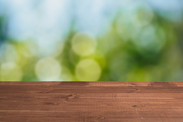 Fototapeta premium Wooden table in front of a blurred background. Perspective brown wood with a blurry multi-colored background - can be used to showcase or assemble your products. Mock up to display the product.