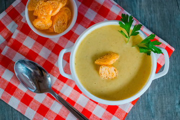 Cream soup of vegetables  in a white bowl and a red and white napkin on a gray background.