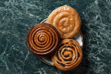 Bun with raisins, cinnamon bun, meat pie on saucer on green marble background