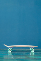 Plastic skateboard on the green floor against blue wall indoors. Side view © Dmitry Zimin