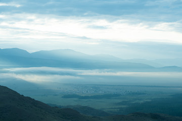 Fototapeta premium clouds and rays of dawn in mountain valley, soft light in early morning, meditation in nature. Gentle hills in bluish haze, silhouettes of mountains