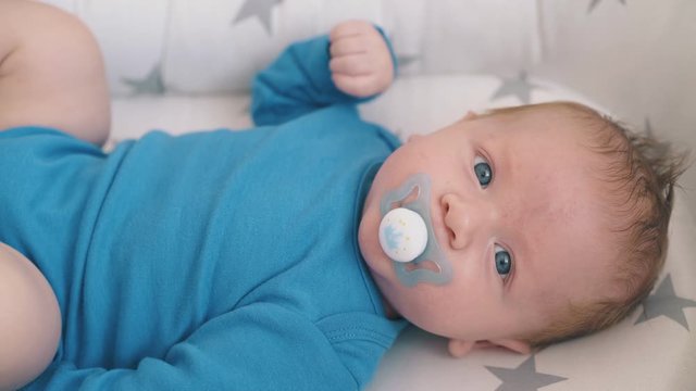 lovely blue eyed baby sucks butterfly shaped dummy in cozy cocoon with star patterns extreme closeup
