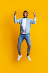 Euphoric afro guy jumping in air, celebrating success over yellow background