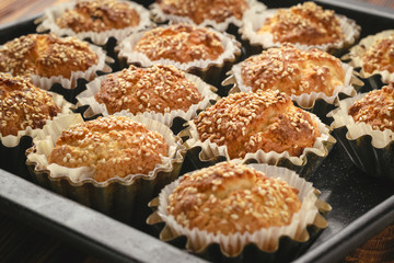 Baked cupcakes with sesame seeds in aluminum molds on a baking sheet