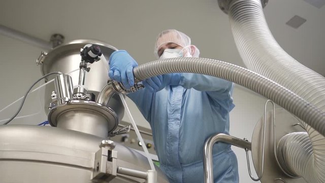 male worker is adjusting metal machine pipe in a workshop of pharmaceutical factory. engineer operating machinery on plant. mixing powder and granules. man turning control process