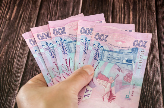 banknotes of 200 hryvnia in hand on a wooden table background.
