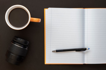 Composition Created Using Coffee cup, Camera Lens, Notebook and Black Pencil on Dark Background