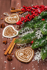 Christmas background. New Year fir tree, dog rose, fresh leaves, crocheted ginger cookies hearts, spices and artificial snow. Wooden boards backdrop