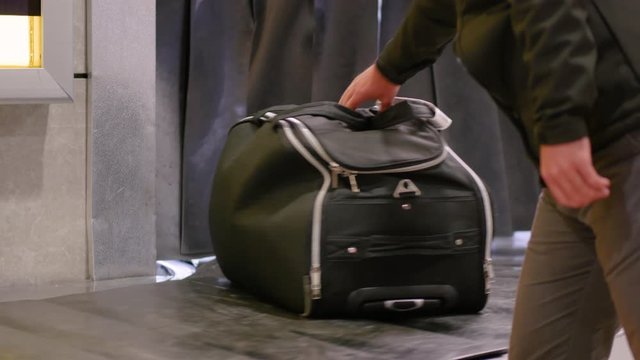 Luggage claim at the airport. A man picks up a bag from a conveyor belt at the baggage reclaim area at an arrival airport.