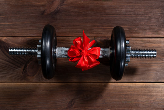 gift - a dumbbell tied with a red ribbon on a dark wooden table