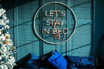 Lazy slogan let's stay in bed on the blue wall next to the bed and the Christmas tree