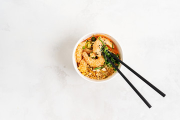 Asian food background with Spicy Shrimp Poke Bowl with rice, seaweeds and sesame seeds, avocado in a lunch box with chopsticks on white. Healthy seafood lunch. Diet food. Top view with copy space.