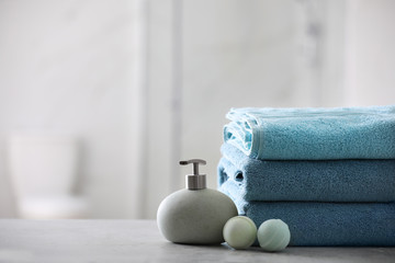 Stack of fresh towels, soap dispenser and bath bombs on table indoors. Space for text
