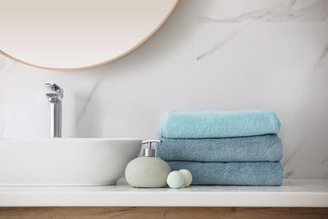 Stack of fresh towels, soap dispenser and bath bombs on countertop  indoors