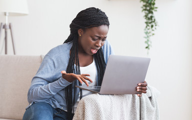 Frustrated afro girl having problems with laptop at home