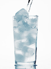 pouring water in a glass full of ice cubes, white background, blue toned object